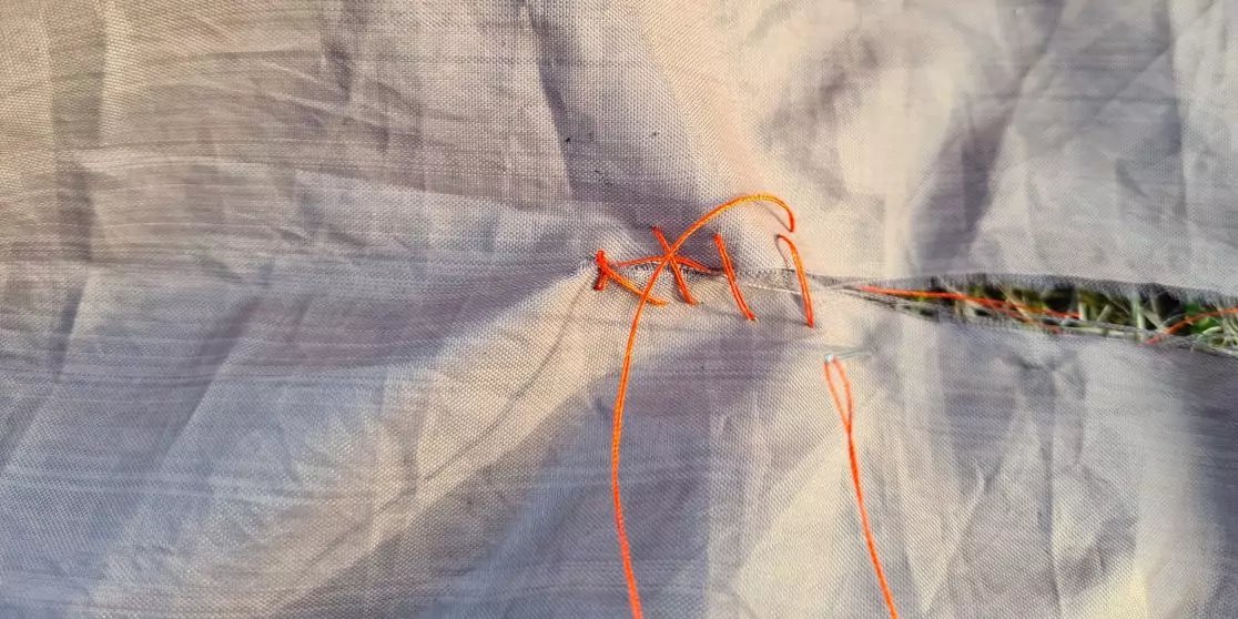 Orangefarbene F&auml;den mit Schlaufen und kleinem Knoten um ein d&uuml;nnes mehrfarbig geflochtenes Seil auf zerknittertem hellgrauem Stoff