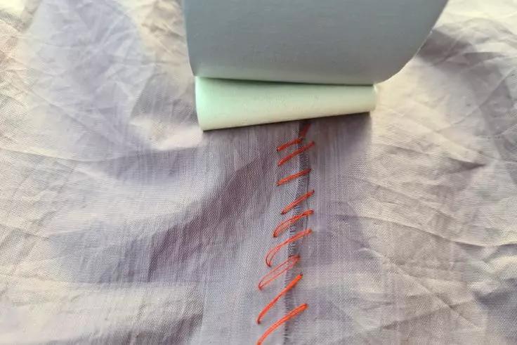 Wei&szlig;e Rolle auf zerknittertem hellviolettem Stoff; darunter rote Zickzack-N&auml;hte