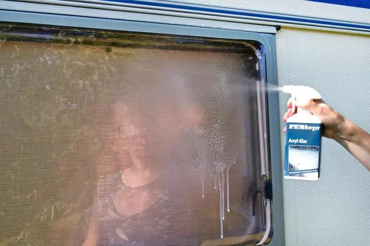 Hand mit Spr&uuml;hdose spr&uuml;ht auf beschlagenes Wohnmobilfenster; hinter dem Glas ist eine unscharfe Person sichtbar