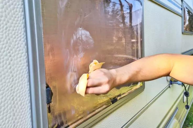 Arm und Hand wischen mit einem gelben Schwamm ein beschlagenes rechteckiges Fenster an einer metallverkleideten Au&szlig;enwand