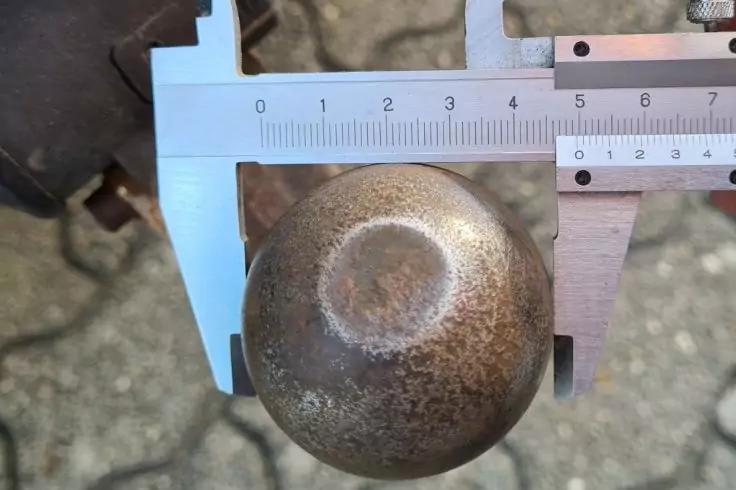 Messschieber umschlie&szlig;t eine runde, rostige Metallkugel; Skala mit Zahlen sichtbar