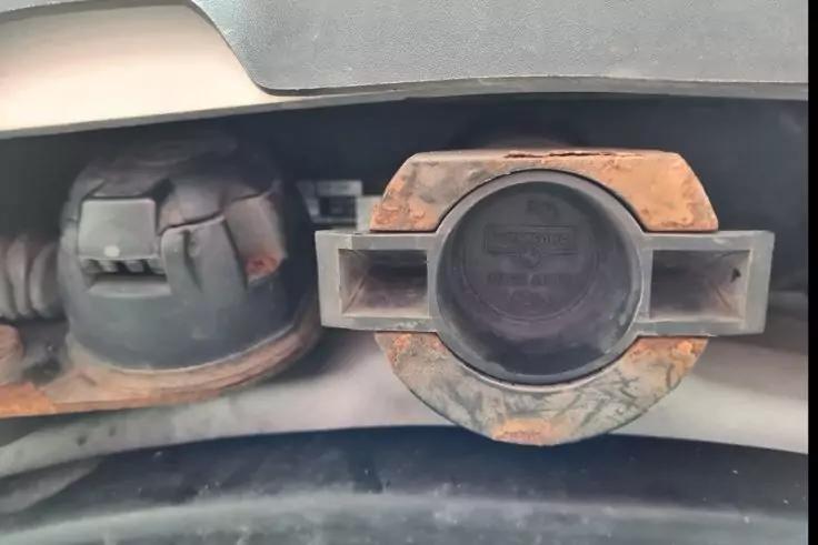 Nahaufnahme von zwei runden Metallteilen mit Rost; rechts ein rundes Metallteil mit rechteckigen Fl&uuml;geln, links ein abgedecktes rundes Metallteil; darunter ein schwarzes Kabel