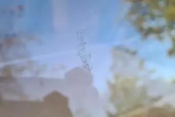 Unscharfes Foto einer transparenten Fl&auml;che mit sichtbaren Flecken; im Hintergrund unscharfe Baumzweige und blauer Himmel