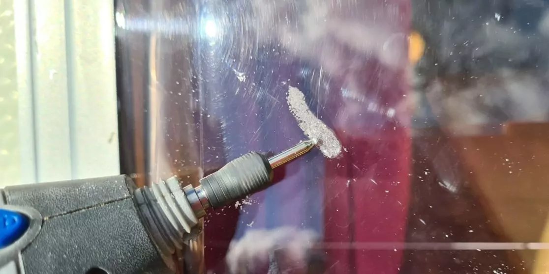 Elektrisches Rotationswerkzeug mit Schleifaufsatz auf einer Glasscheibe; Fenster und Reflexionen im Hintergrund