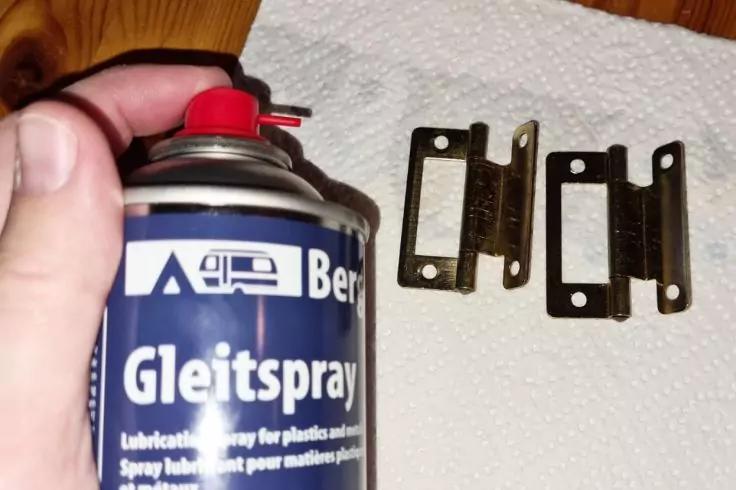 Hand h&auml;lt eine Spraydose mit Aufschrift "Gleitspray"; daneben drei metallene Platten mit rechteckigen Aussparungen auf einem Papiertuch