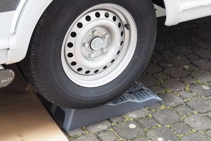 Reifen eines weißen Fahrzeugs auf einem schwarzen Radkeil auf Kopfsteinpflaster