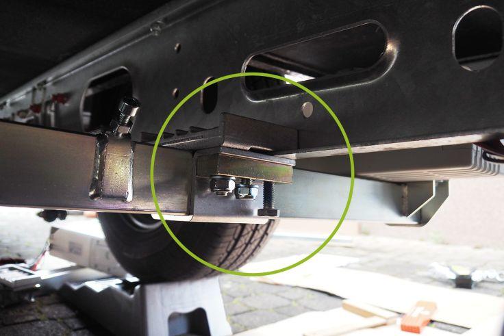 Unterseite eines Fahrgestells mit Reifen und geschraubter Metallhalterung im grünen Kreis