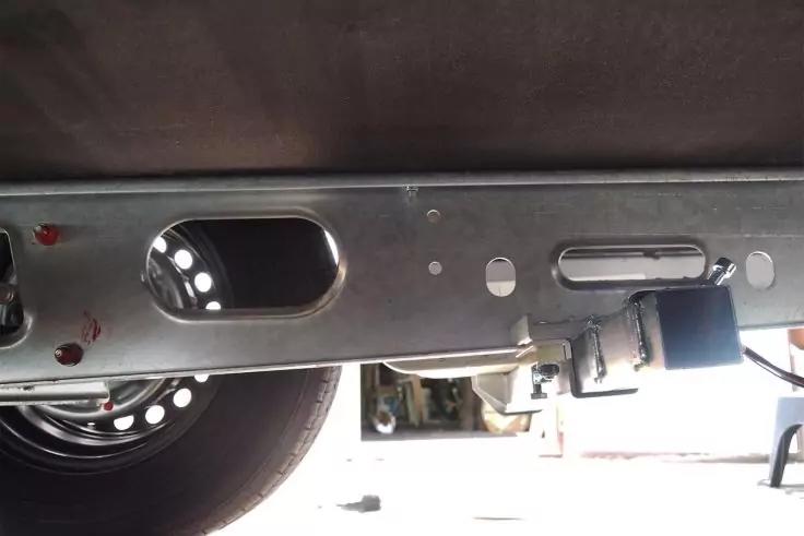 Unterseite mit links sichtbarem Rad, Metallrahmen mit Aussparungen und Schrauben, kleine rote Farbsprenkel, heller Hintergrund