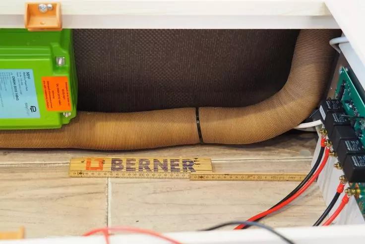 Braunes flexibles Rohr, Holzlineal mit Aufschrift 'BERNER', grünes Gehäuse links, Leiterplatte mit roten und schwarzen Kabeln rechts, helle Bodenfliesen