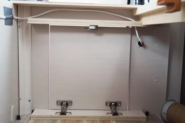 Offenes Holzfach mit zwei Metallscharnieren, oberer Ablageboden, weißes Kabel rechts