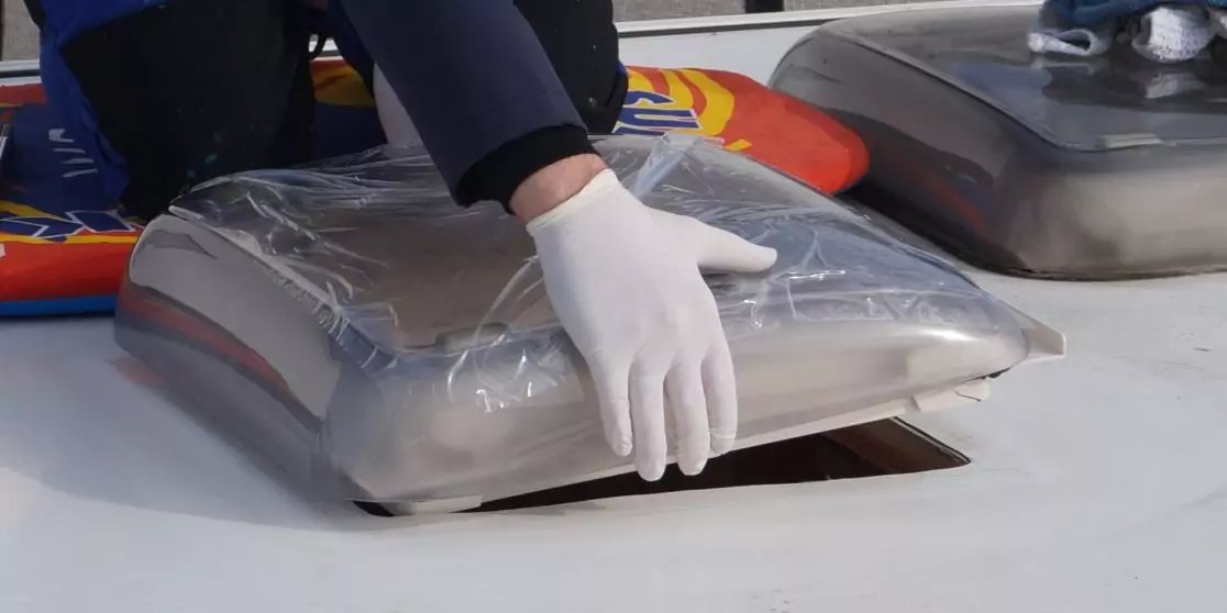 Hand mit wei&szlig;em Handschuh auf einer rechteckigen, durchsichtigen Luke auf wei&szlig;er Oberfl&auml;che; nebenan eine zweite &auml;hnliche Luke sichtbar