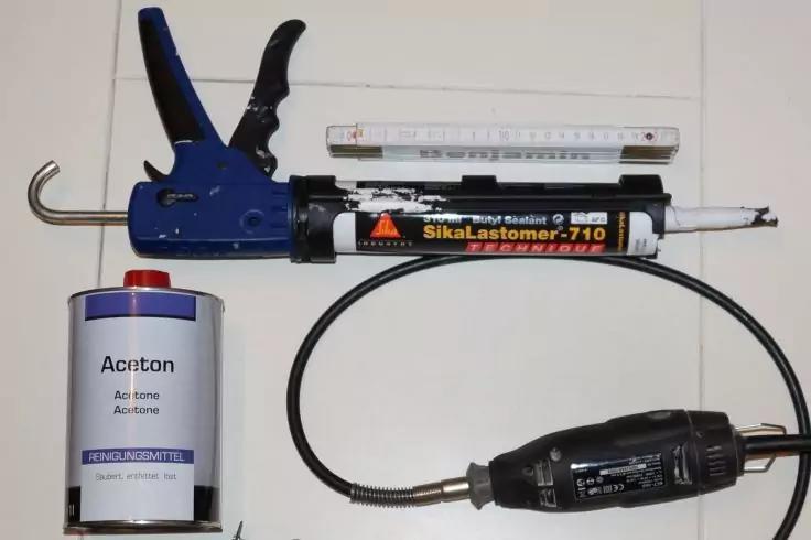 Blaue Kartuschenpistole, schwarze Kartusche mit Aufschrift 'SikaLastomer-710' und wei&szlig;er Mischd&uuml;se, Metalllineal, Blechkanne mit Aufschrift 'Aceton' und blauem Verschluss, flexible Welle mit schwarzem Handst&uuml;ck auf wei&szlig;em Untergrund