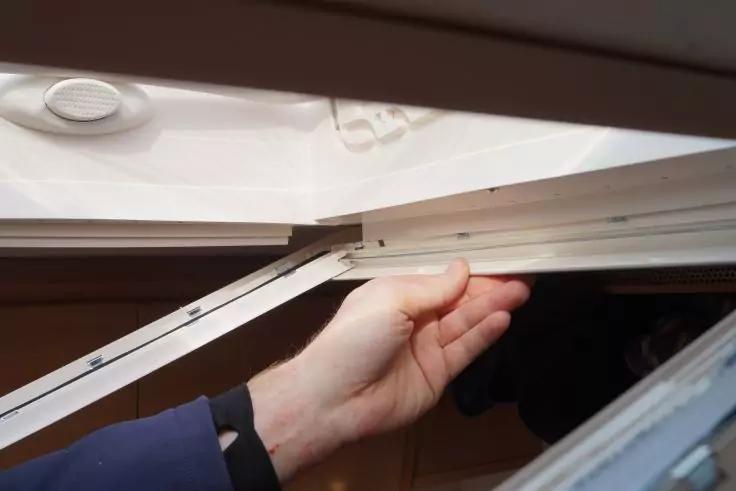 Hand h&auml;lt wei&szlig;en Fensterrahmen eines ge&ouml;ffneten Dachfensters; oben links runde L&uuml;ftungs&ouml;ffnung in der Decke