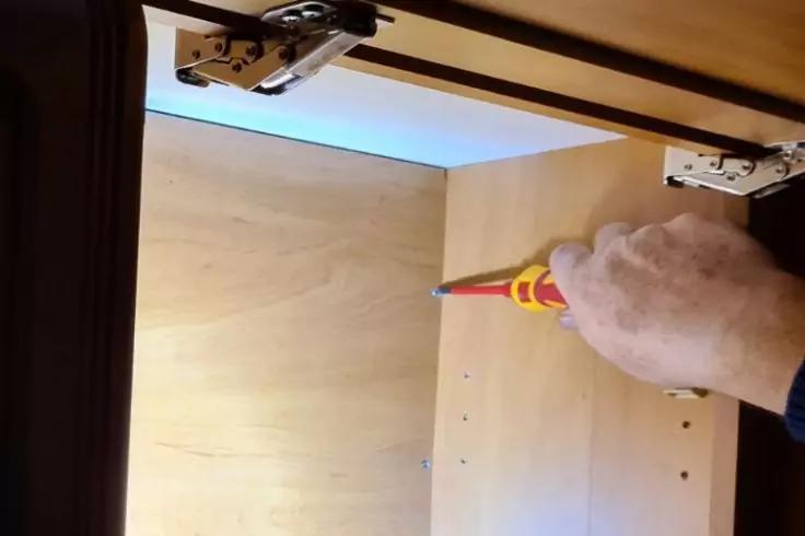 Hand h&auml;lt Schraubendreher in offenem Holzschrank, oben sichtbare Scharniere