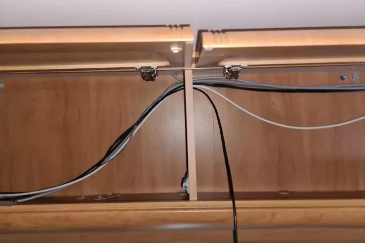 Holzfl&auml;che mit zwei senkrechten Platten, eine schmale &Ouml;ffnung dazwischen, mehrere schwarze und wei&szlig;e Kabel, Metallklemmen und Schrauben sichtbar