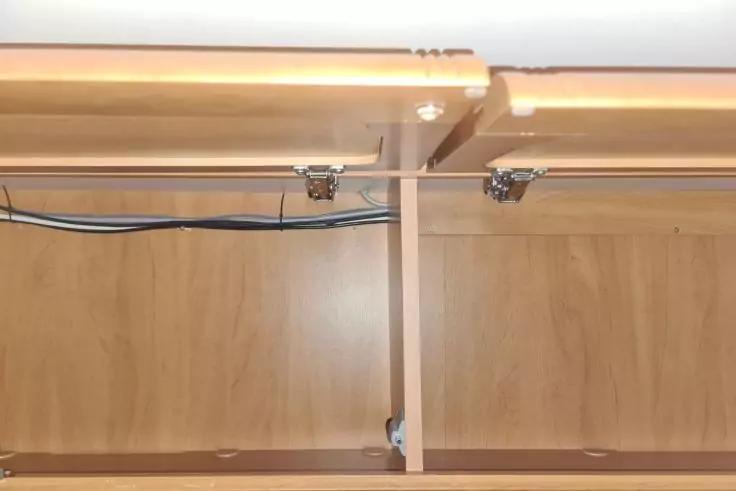 Innenansicht eines Holzfachs mit vertikalem Trennbrett in der Mitte, sichtbaren Kabeln entlang der oberen R&uuml;ckwand, zwei Metallbeschl&auml;gen an der Oberkante und einer Lichtleiste oben