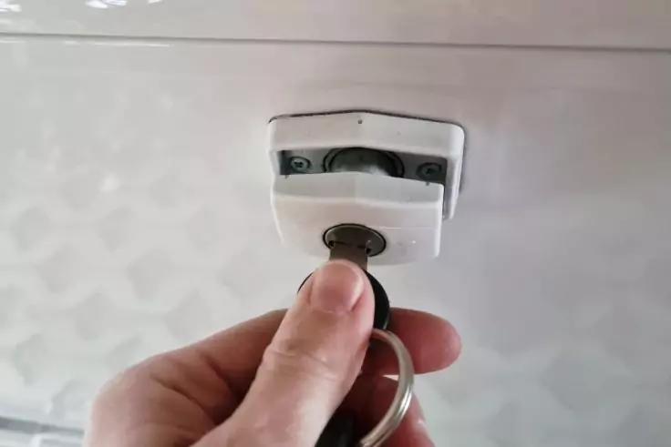 Hand h&auml;lt Schl&uuml;ssel mit Schl&uuml;sselring, Schl&uuml;ssel steckt in Zylinderschloss an wei&szlig;er Oberfl&auml;che