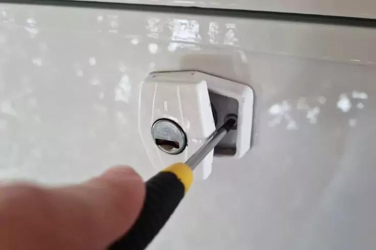 Hand h&auml;lt Schraubendreher an einer Schraube eines wei&szlig;en Schlosses auf einer wei&szlig;en Oberfl&auml;che