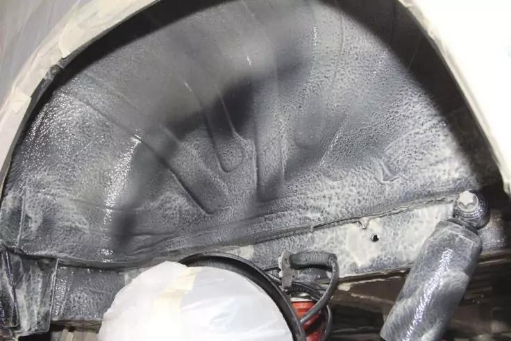 Geschwungene dunkle, texturierte Innenfl&auml;che mit Schrauben und Befestigungsbohrungen; rechts ein silbernes Rohr; unten links wei&szlig;e Plastikfolie und rotes Kabel