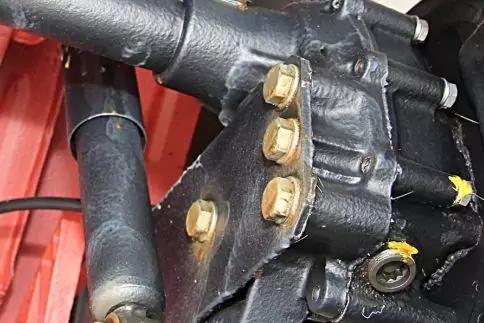 Nahaufnahme eines schwarzen Metallteils mit vier goldenen Sechskantbolzen, gelben Markierungen, Schwei&szlig;n&auml;hten und rotem Hintergrund