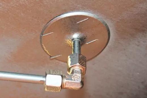 Metallrohr mit rechtwinkligem Fitting und Mutter, befestigt an einer runden Metallplatte an einer braunen Oberfl&auml;che