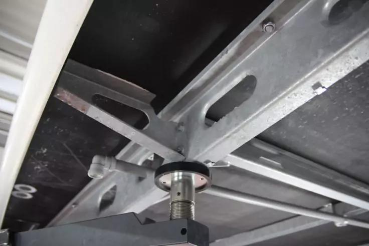 Untersicht von Metallstreben mit ovalen Aussparungen, einer zylindrischen Welle mit schwarzem Ring und sichtbaren Schrauben