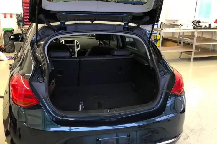 Geöffneter Kofferraum eines dunklen Hatchback-Autos in einer Werkstatt, leerer Laderaum, sichtbare Rücksitze, geöffnete Heckklappe, Werkbank im Hintergrund