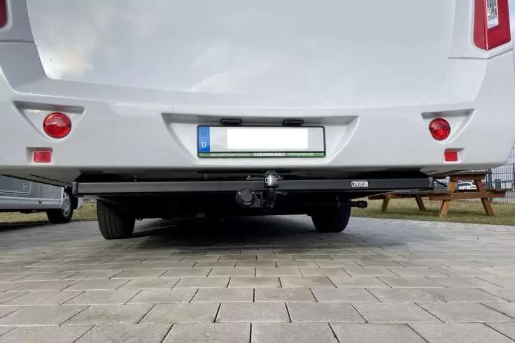 Heck eines weißen Fahrzeugs mit Anhängerkupplung, sichtbarem Kennzeichen und gepflastertem Untergrund