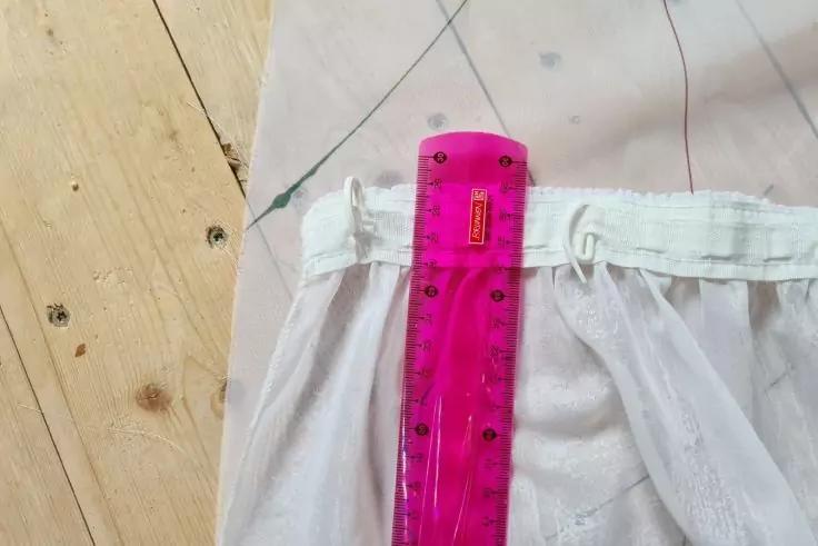 Pink-transparentes Plastiklineal liegt auf wei&szlig;em, gerafftem Stoff mit Bund; links heller Holzboden; oben Musterpapier mit Markierungen