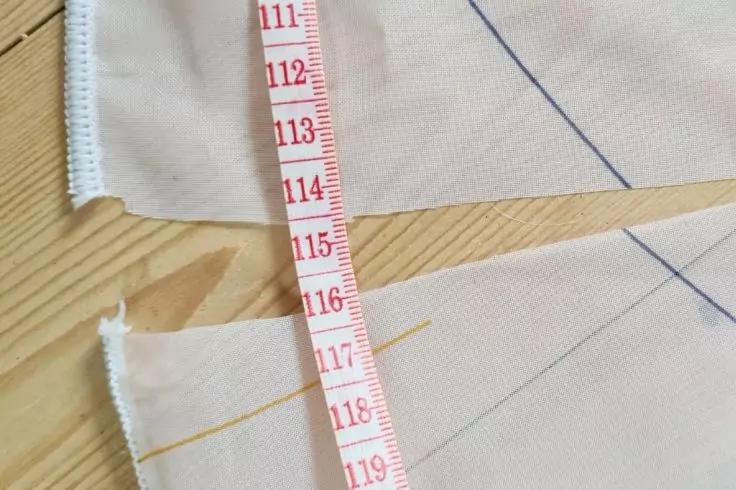 Ma&szlig;band mit roten Zahlen liegt quer auf zwei hellrosa Stoffst&uuml;cken mit blauen und gelben Markierungslinien auf einem hellen Holztisch