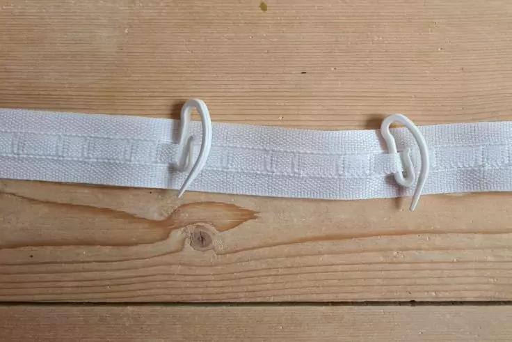 Wei&szlig;er Stoffstreifen mit zwei wei&szlig;en Plastikhaken auf hellem Holzbrett