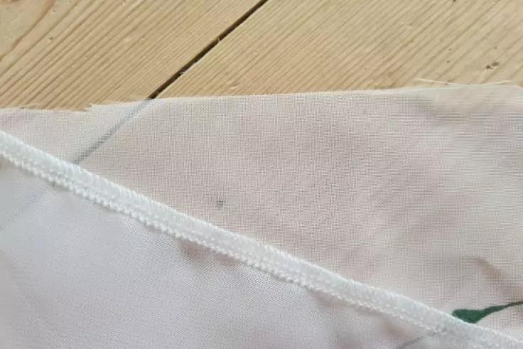 Nahaufnahme eines wei&szlig;en Stoffes mit sichtbarer Naht, kleinen dunklen Flecken, einem gr&uuml;nen Fleck am Rand und einem Holzbrett im oberen Bereich