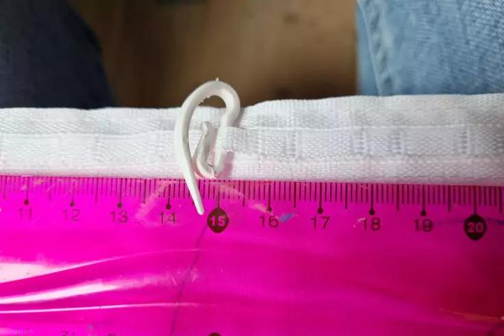 Wei&szlig;es Stoffband mit angen&auml;hter Schlaufe, durch die ein wei&szlig;er Kunststoffhaken gesteckt ist; darunter ein transparentes rosa Lineal mit Zentimeter-Markierungen, im Hintergrund Holzboden und Jeansstoff