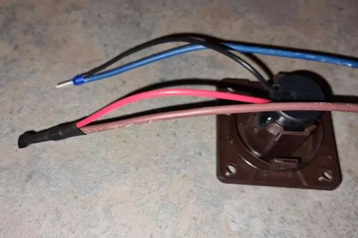 Braune quadratische Kunststoffhalterung mit rundem Bauteil und mehreren isolierten Dr&auml;hten in Rot, Blau und Schwarz; an einem blauen Draht ist das Ende abisoliert