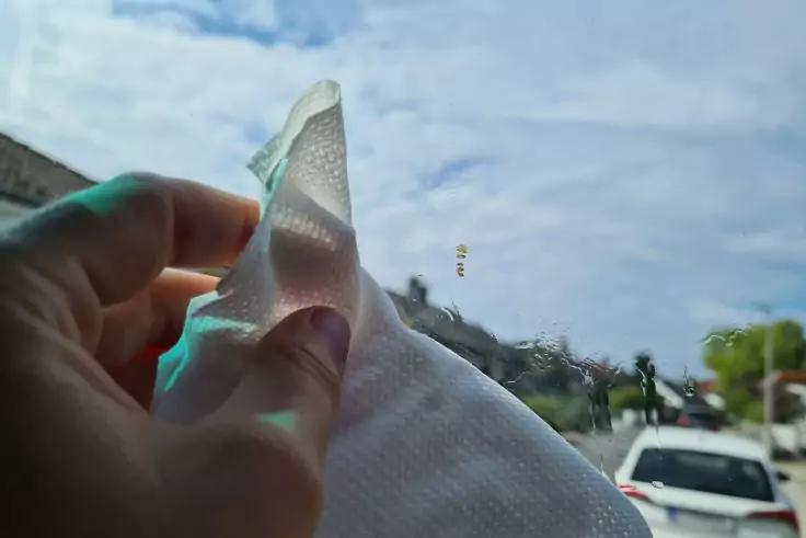 Hand h&auml;lt im Vordergrund ein wei&szlig;es Papiertuch; im Hintergrund Stra&szlig;e mit wei&szlig;em Auto, H&auml;usern, B&auml;umen und bew&ouml;lktem Himmel