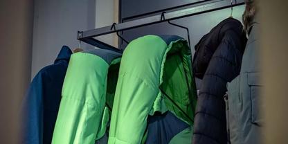 Mehrere Jacken an einer Wandgarderobe, darunter gr&uuml;ne Jacken und dunkle M&auml;ntel