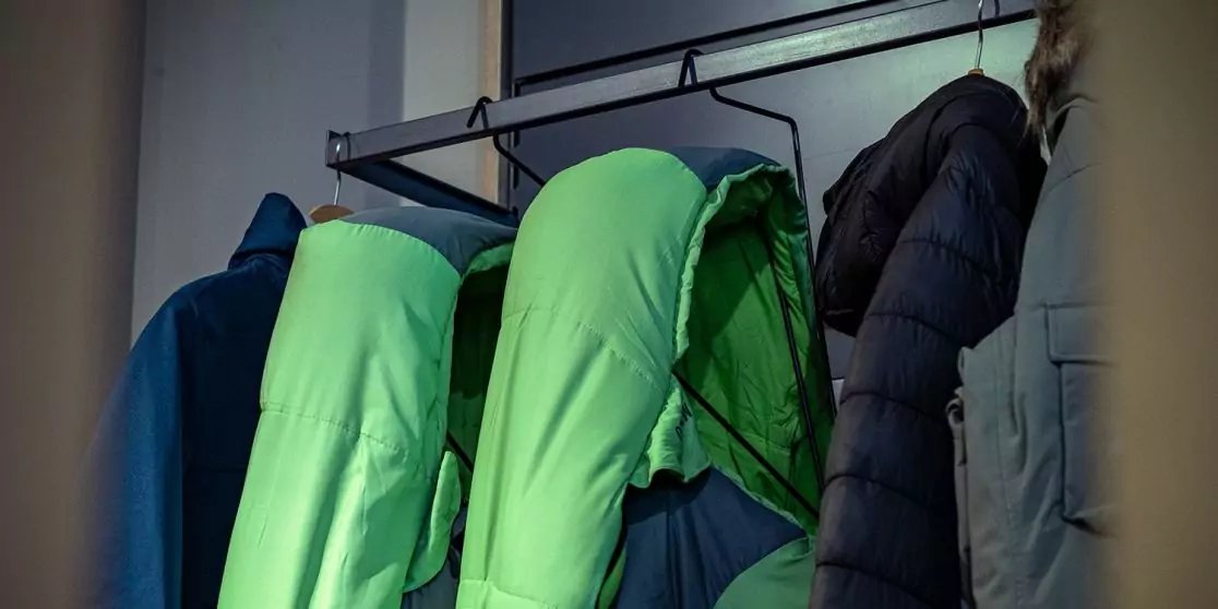 Mehrere Jacken an einer Wandgarderobe, darunter gr&uuml;ne Jacken und dunkle M&auml;ntel