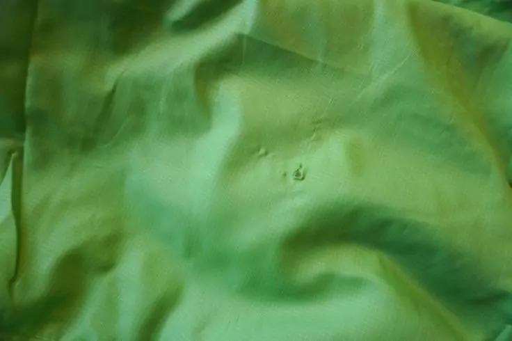 Gr&uuml;ner Stoff mit Falten und kleinem Loch in der Bildmitte