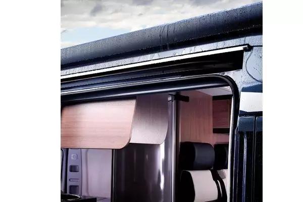 Geöffnete Seitentür eines Fahrzeugs, sichtbar: Holzschrank, gepolsterter Sitz mit Kopfstütze und Türrahmen