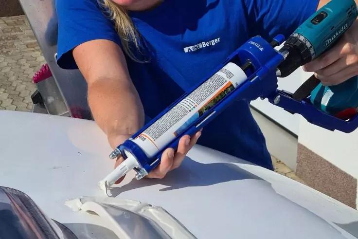 Person in blauem T-Shirt h&auml;lt eine Kartuschenpresse und tr&auml;gt wei&szlig;e Dichtmasse auf eine wei&szlig;e, gew&ouml;lbte Oberfl&auml;che auf