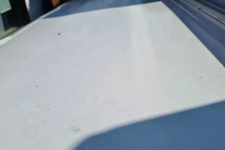 Wei&szlig;e flache Fl&auml;che mit kleinen Schmutzpartikeln, blauem Rand rechts, dunklem Schatten im Vordergrund und unscharfem Hintergrund