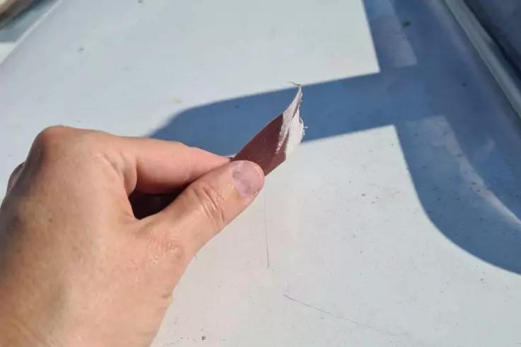 Hand h&auml;lt eine abgel&ouml;ste, gebogene Farbschicht &uuml;ber einer wei&szlig;en Oberfl&auml;che mit Schatten