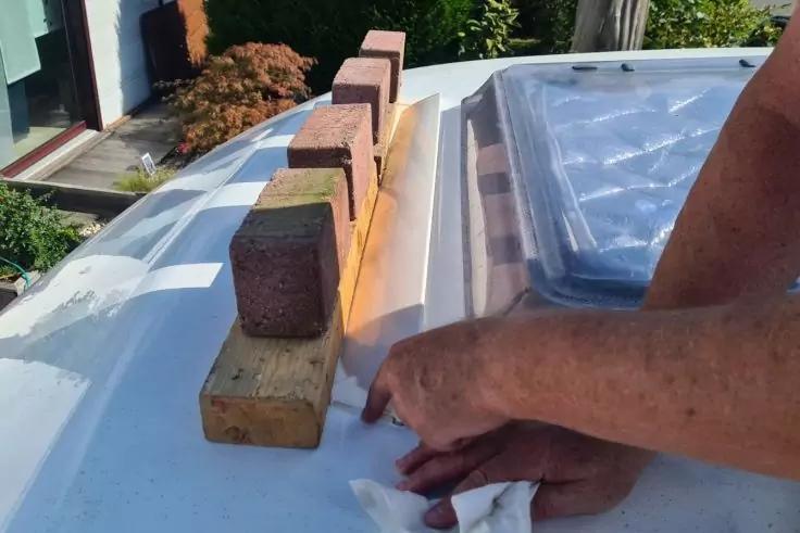 H&auml;nde und Unterarme &uuml;ber einer wei&szlig;en Fl&auml;che mit einer rechteckigen transparenten Abdeckung; Holzkl&ouml;tze mit darauf gestapelten Ziegeln