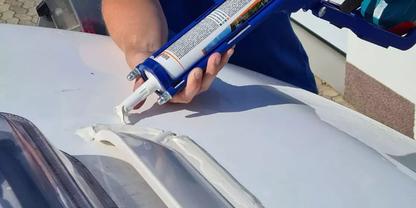 H&auml;nde halten eine blaue Kartuschenpistole, aus der wei&szlig;e Paste auf eine wei&szlig;e, gew&ouml;lbte Fl&auml;che mit drei Rippen gedr&uuml;ckt wird; Wand im Hintergrund