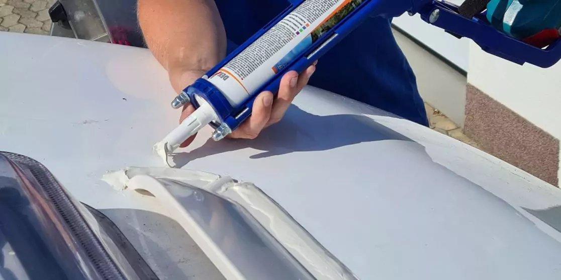 H&auml;nde halten eine blaue Kartuschenpistole, aus der wei&szlig;e Paste auf eine wei&szlig;e, gew&ouml;lbte Fl&auml;che mit drei Rippen gedr&uuml;ckt wird; Wand im Hintergrund