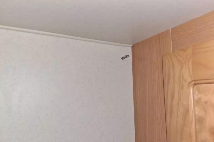 Obere Zimmerecke mit wei&szlig;er Decke und Wand, rechts Holz-T&uuml;rrahmen und kleines metallisches Befestigungsteil an der Wand