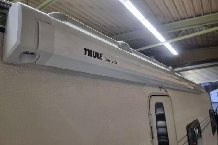 Wei&szlig;es Thule Omnistor-Geh&auml;use an der Seitenwand eines Wohnmobils, Fenster mit Lamellen und Hallendecke mit Leuchten sichtbar