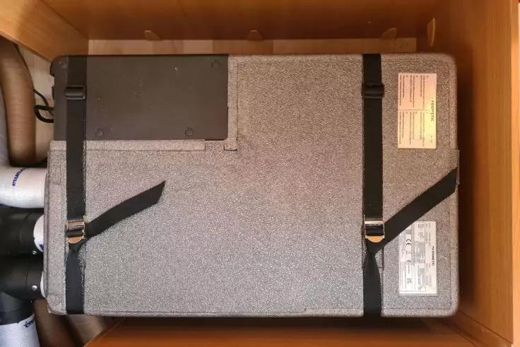 Graues rechteckiges Ger&auml;t in einem Holzschrank, zwei schwarze Gurte, Aufkleber und Schl&auml;uche links