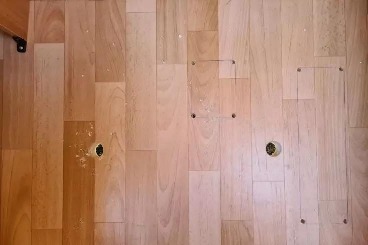 Holzboden mit zwei runden L&ouml;chern, mehreren kleinen L&ouml;chern, rechteckigen Umrissen und wei&szlig;en Sprenkeln auf hellen Dielen