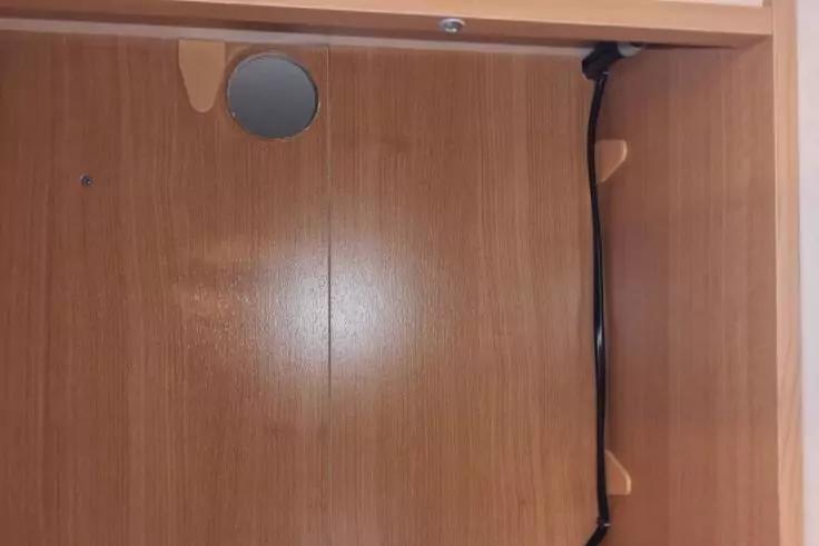 Innenraum eines Holzschranks mit rundem Kabeldurchlass oben links und einem schwarzen Kabel, das an der rechten Innenwand mit beige-farbenen Halterungen verl&auml;uft